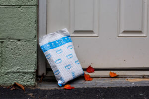 A square white and blue Amazon package sitting on a doorstep, surrounded by orange fall leaves.