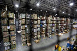 A FORKLIFT TRUCK DRIVES PAST HUGE STACKS OF GOODS IN A WAREHOUSE