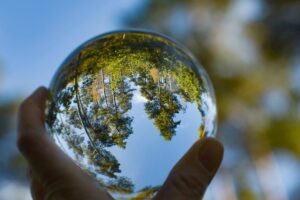 A HAND HOLDS UP A GLASS BALL REFLECTING AN IMAGE OF TREES UPSIDE DOWN