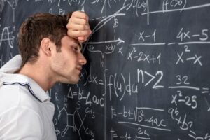 A MAN LEANS WITH HIS EYES CLOSED IN DESPAIR ON A BLACKBOARD FULL OF MATHEMATICAL EQUATIONS