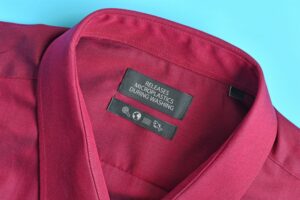A BURGUNDY SHIRT BEARS A LABEL THAT READS RELEASES MICROPLASTICS DURING WASHING