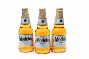 THREE BOTTLES OF MODELO BEER STAND IN A ROW ON A WHITE BACKGROUND