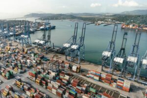 A LARGE PORT WITH CRANES AND STACKS OF CONTAINERS IS SEEN FROM ABOVE