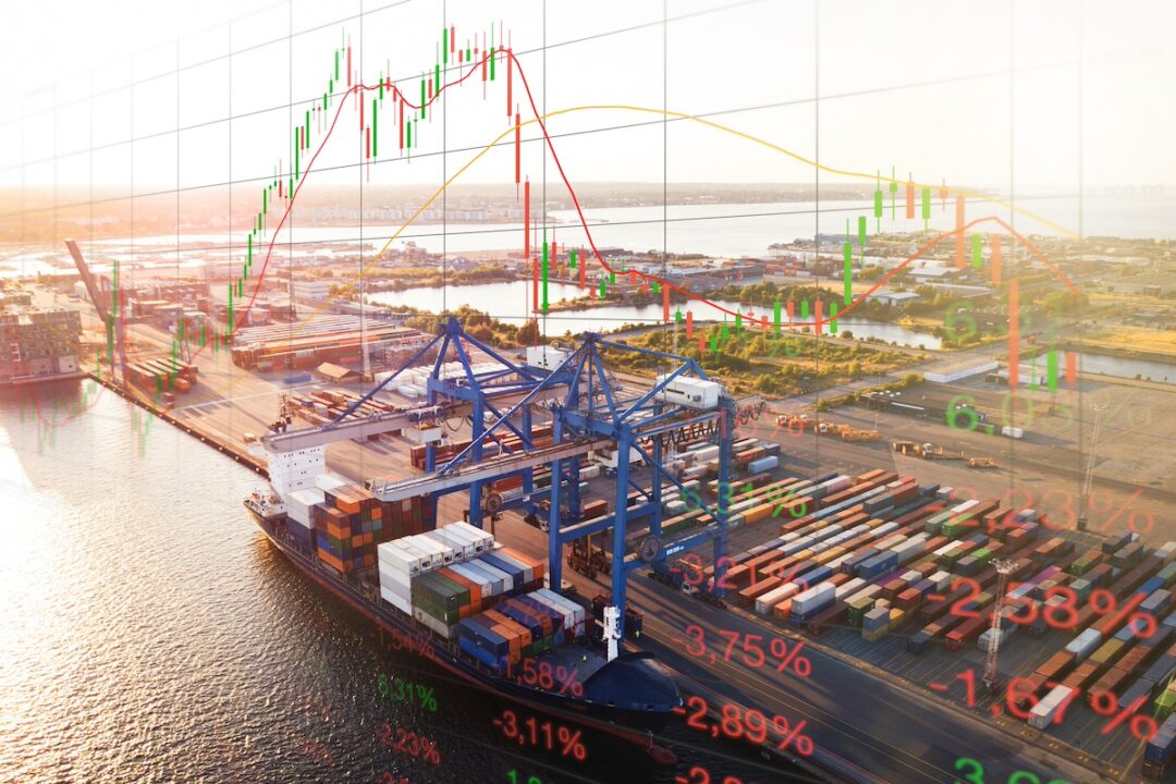 A black container ship stacked with containers docked under two blue cranes, with a green and red line graph superimposed over the skyline