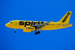 A BRIGHT YELLOW SPIRIT AIRLINES PLANE FLIES IN AN ELECTRIC BLUE SKY