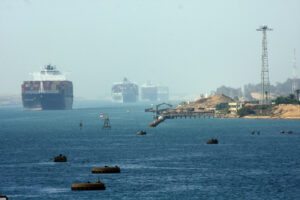 THREE LARGE CONTAINER SHIPS CAN BE SEEN TRAVELING ON A BODY OF WATER NEAR A SMALL HARBOR.