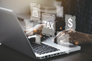 A PAIR OF HANDS WORKS AT A LAPTOP, SURROUNDED BY FINANCIAL SYMBOLS